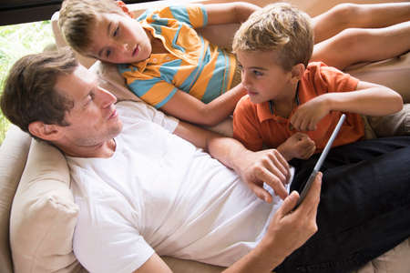 Man and two sons using digital tablet touchscreen on sofa