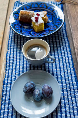 Table with bowl of cake, black coffee and plumsの写真素材
