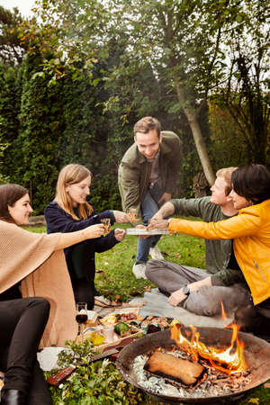 Group of friends enjoying picnic around fire pit in gardenの写真素材