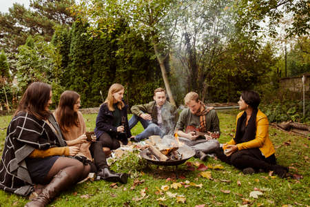 Group of friends having picnic around fire pit in garden