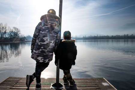 Italy, Rear view of brothers (4-5, 11-12) on pier on calm lakeの写真素材