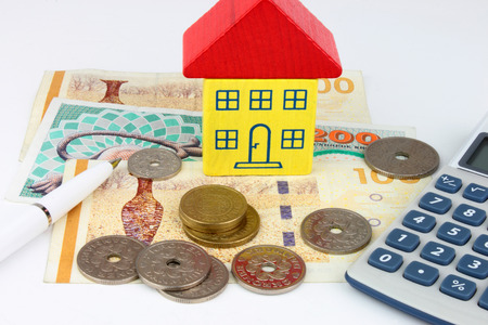A toy house sitting on Danish Kroner notes, with coins and a calculatorの写真素材
