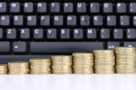 Stacks of coins in a rising column against a backdrop of a computer keyboardの写真素材