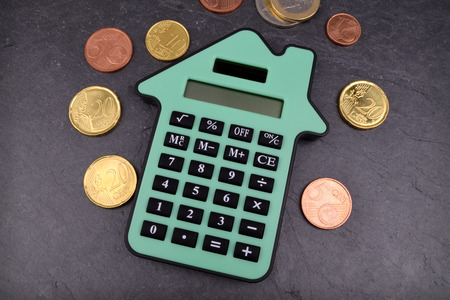 A house shaped calculator against a slate background, with Euro coins around it.の写真素材