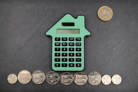 A house shaped calculator against a slate background, with Sterling coins for gound and sun.の写真素材