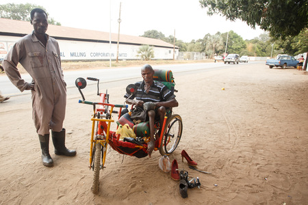 LIVINGSTONE - OCTOBER 14 2013: Local disabled man with an adapted wheelchair sets up successful shoe repair business in Livingstone, Zambia, Africaのeditorial素材