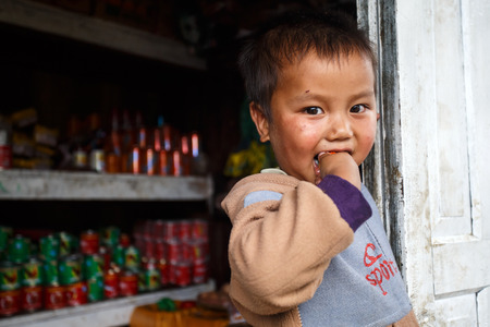 FALAM, MYANMAR - JUNE 17 2015: Local cute boy stands at convenience store entrance at the start of the monsoon season in the recently opened to tourists Chin State region of Western Myanmar (Burma)のeditorial素材