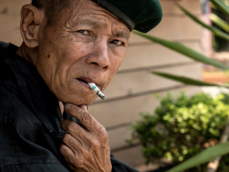 MAE TAN NOI, THAILAND - MARCH 22 2015: Elderly Thai Man, sits and smokes at remote train station Mae Tan Noi on one of the hottest recorded days in Northern Thailand.のeditorial素材