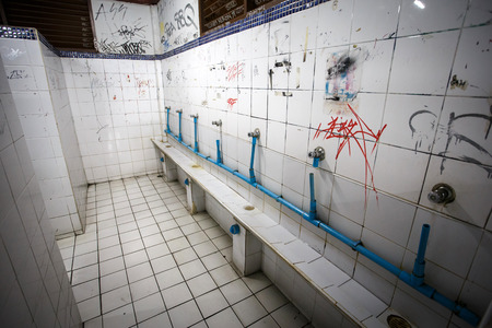 Urinal in an urban ghetto washroom / restroom with dirty grungy graffiti wallsのeditorial素材