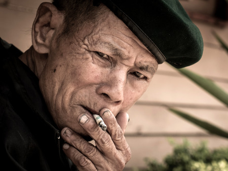 MAE TAN NOI, THAILAND - MARCH 22 2015: Elderly Thai Man, sits and smokes at remote train station Mae Tan Noi on one of the hottest recorded days in Northern Thailand.のeditorial素材