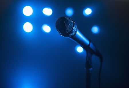 A close up view of a microphone and stand.  The background is blue and has several spotlights. Horizontally framed shot.の写真素材