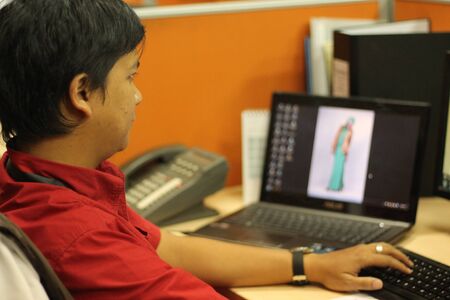 Office workers in a red shirts working in an office in orange cluster in the front of computer and laptopの写真素材