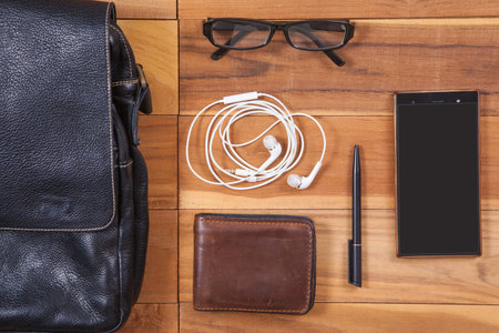 Travel concept - leather bag, glasses, earphones, wallet, pen, mobile phone on wooden deskの写真素材