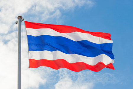 waving Thai flag of Thailand with blue sky background.