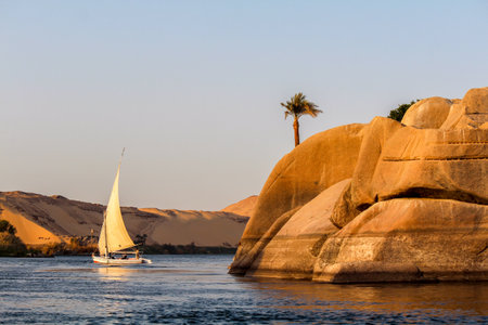 Sailboat on the Nile river at sunset, rock with ancient carvings in the front, Egyptの写真素材