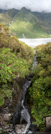 Vertical panoramic view of mountain stream flowing into glacial valley of Franz Josef Glacier National Park, New Zealandの写真素材