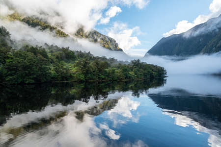 A new morning dawning at Doutful Sound, clouds hanging low in the mountains, South Island of New Zealandの写真素材