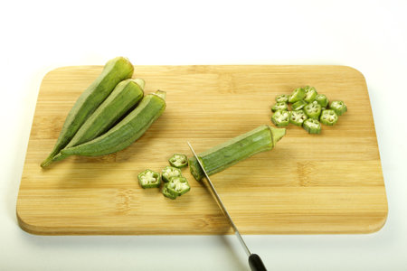 Fresh raw okra being chopped with a knife on a chopping board isolated on white background
の写真素材