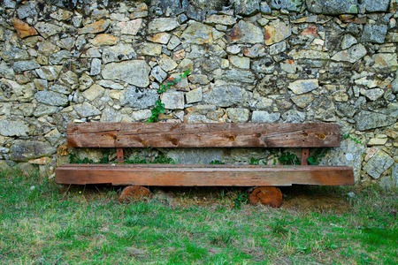 Rural wooden bench in front of a rock wall place on top of green grass.の写真素材