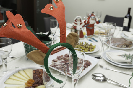 A reindeer diadem place on Champagne glases on a table set for christmas dinner.  There are dishes and christmas decor in the background.の写真素材