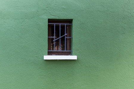 A single wooden window with metal bars on a green facade.の写真素材