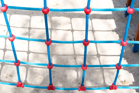 Close-up of climbing wall made of ropes at playground casting shadow on sandy groundの写真素材