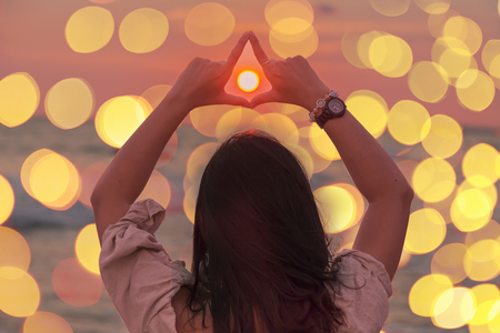 Asian girl standing back Sunset view with bokeh lighting.Extending two arms above the head the sun in the handの写真素材