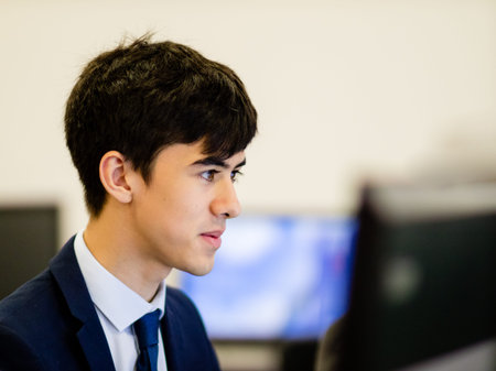 A young man of Asian heritage focussing on his computer monitor