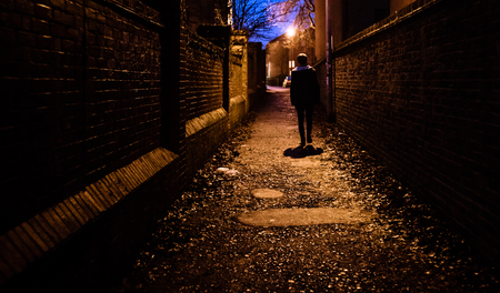 A young man walking home alone at night through a dark alleyway in the UK.の写真素材