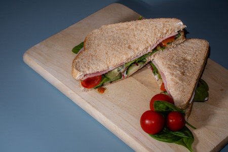 A ham and salad sandwich cut in half with blue in the background