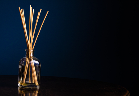Reed diffusers in a small glass bottle on a table with a navy blue background with copy space on the rightの写真素材