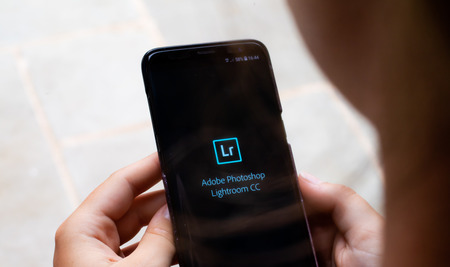 Lincoln, United Kingdom - 07/16/2018: The load screen for Adobe Photoshop Lightroom CC held by a young girl about to edit their photos on the go.のeditorial素材