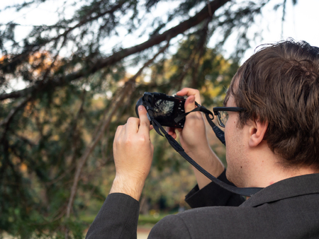 A man taking a picture of trees on his digital camera.の写真素材