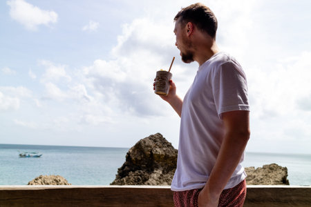 A young man drinking a tropical cocktail while looking at the sea