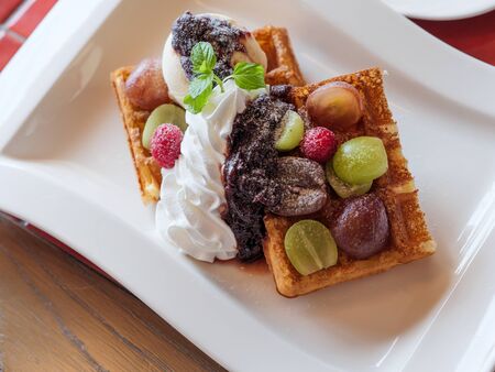 Delicious waffles with fresh fruits, ice cream and whipped cream on a white plateの写真素材