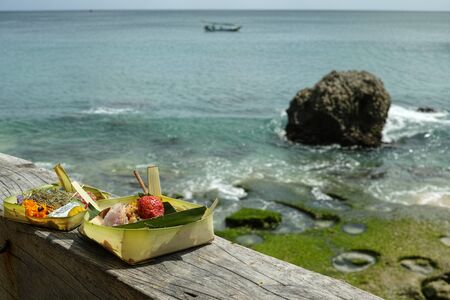 Balinese religious offerings of fruit and incense in front of the tropical coastlineの写真素材