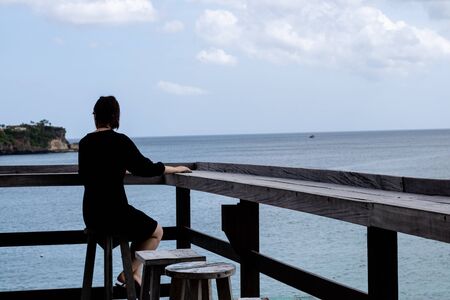 A young Asian woman sitting at a deck and enjoying coastal views in a tropical destinationの写真素材