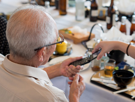 An elderly Asian man struggling to use an old fashioned flip phone