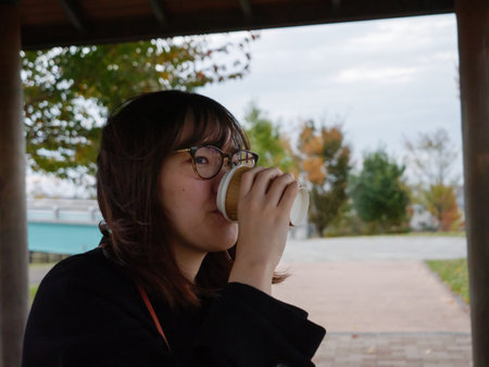 A beautiful Japanese lady drinking coffee in a parkの写真素材