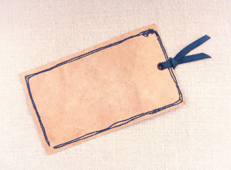 An old vintage like tag with a ribbon lying on a cross stitched fabric 