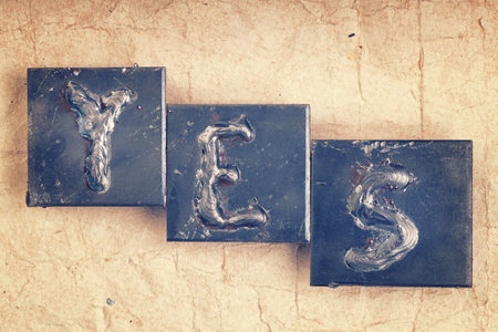 The word "YES" made from metal letters on an old vintage paper backgroundの写真素材