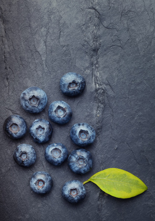 A bunch of delicious blueberries with green leaf on a  black vintage slate of tileの写真素材