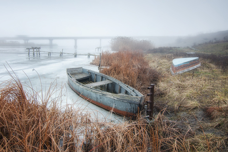The boat is on the snowy bank of the river in winterの写真素材