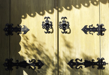 Yellow old wooden church door with metal design for decoration, Ancient church gate with black iron pattern, and shadowsの写真素材