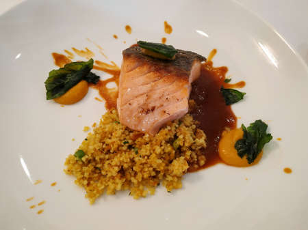 Grilled salmon fillet with couscous, spinach and Biscayne sauce served on a white plateの写真素材