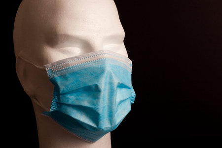 White bust of mannequin with blue hygienic mask on black background