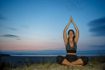 Silhouette of young woman practicing yoga, lotus position, and meditating on the beachの写真素材