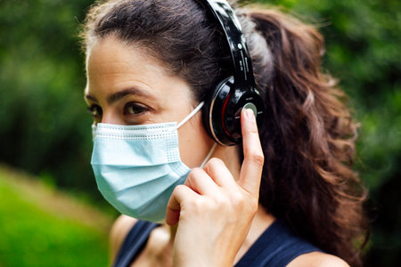 Happy girl with mask in listen music in headphones. Fit your body. Playlist for training in a park