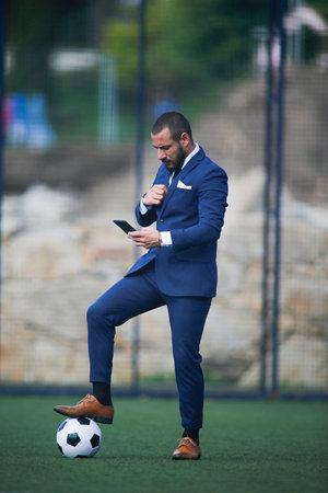 businessman with a ball on his foot chatting with the smartphone inside a soccer fieldの写真素材