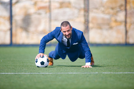 flexed businessman leaning on a ball inside a soccer fieldの写真素材